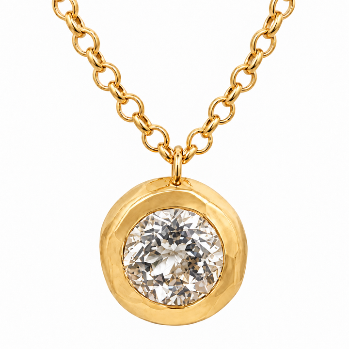 A gold pendant necklace featuring a round bezel-set clear gemstone on a delicate gold chain, shown against a plain white background.