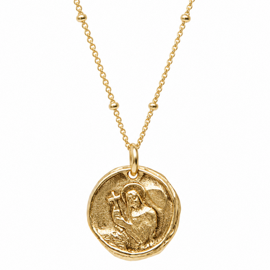 A gold coin pendant necklace featuring an embossed religious figure holding a cross, suspended from a delicate gold chain on a solid white background.