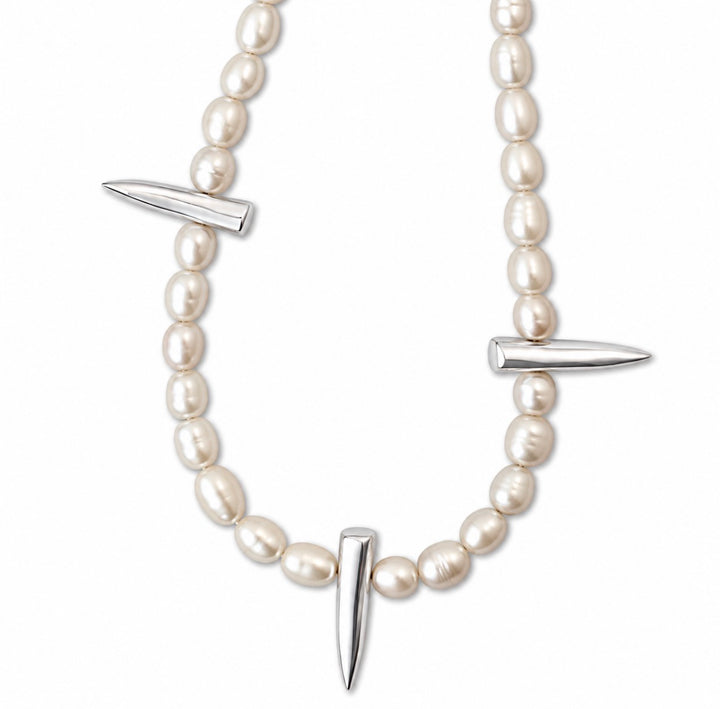 A pearl beaded necklace with three polished silver-toned spike accents, displayed on a clean white background.