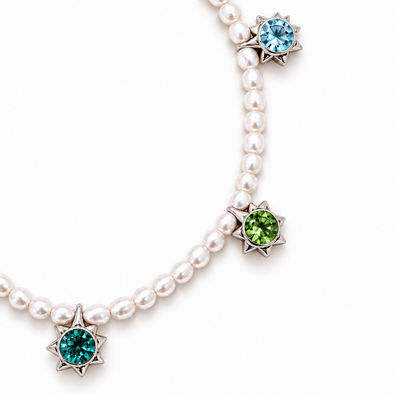 A pearl necklace with three star-shaped silver pendants, each set with a round gemstone in a different color: light blue, green, and teal, on a white background.