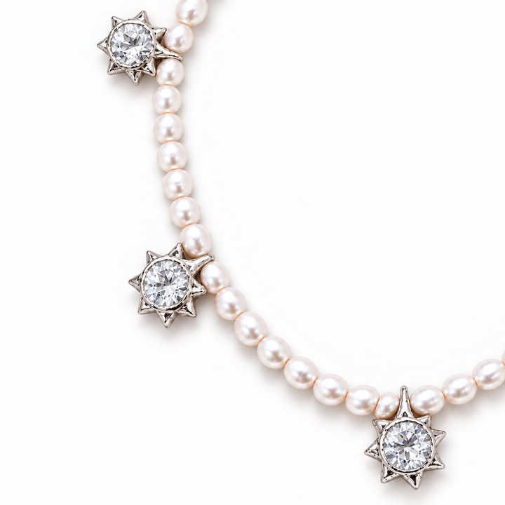 A pearl necklace with silver starburst settings holding round clear gemstones, shown on a clean white background.