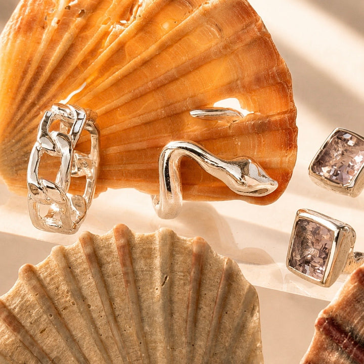 Silver earrings with a textured design on a background of seashells.
