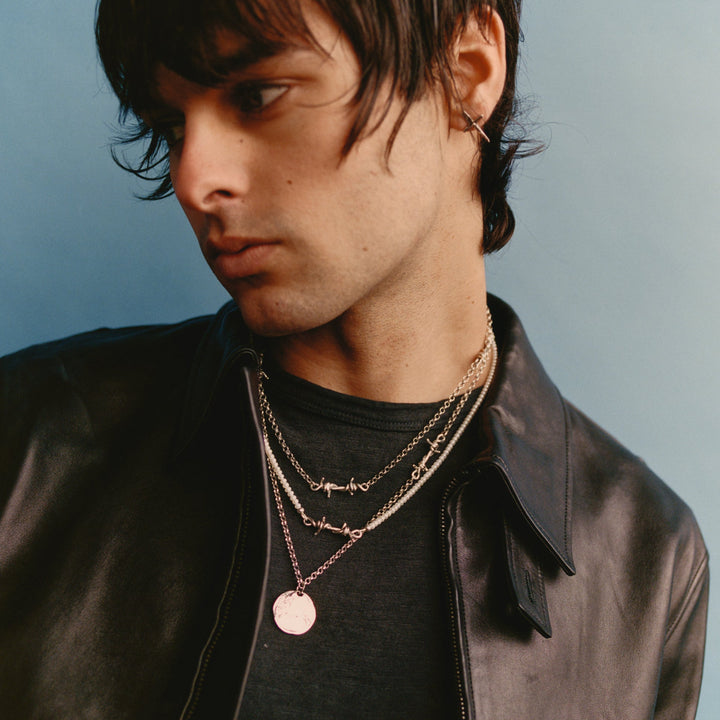 Man wearing a black leather jacket and layered necklaces against a light blue background