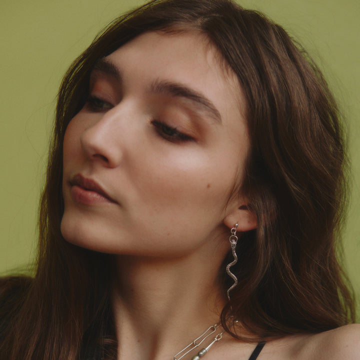 Woman wearing a black top and multiple necklaces with a green background