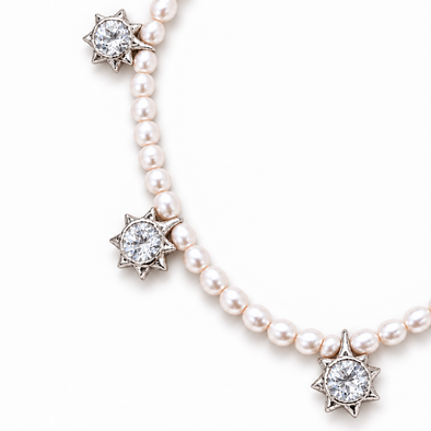 A pearl necklace with silver starburst settings holding round clear gemstones, shown on a clean white background.