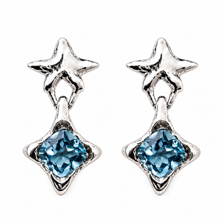 A pair of silver dangle earrings featuring a textured starburst top and a faceted light blue gemstone in a four-pointed starburst shape below, set against a plain white background.