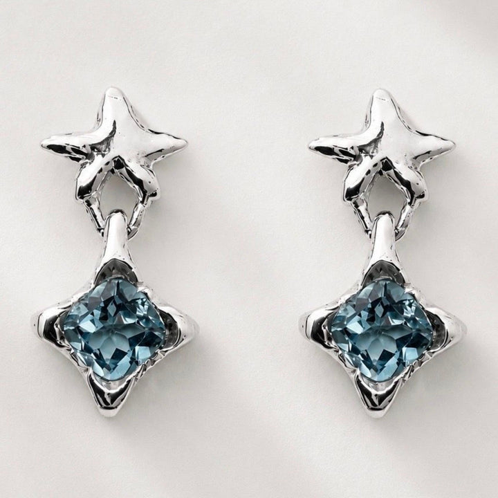 A pair of silver star dangle earrings with faceted light blue gemstones, displayed on a clean white background.