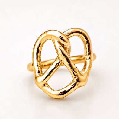 A gold ring designed in the shape of a pretzel, featuring a polished, textured finish on a clean white background.