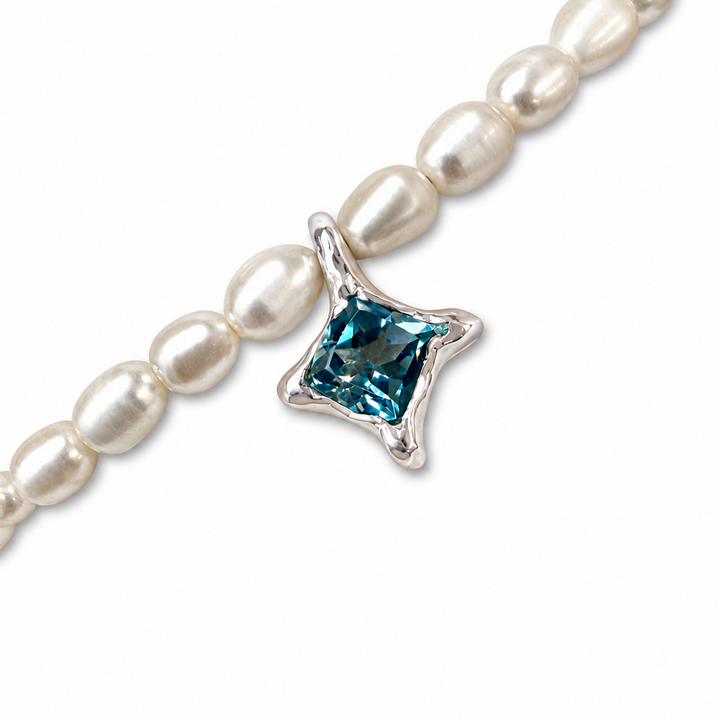 A close-up of a pearl beaded bracelet featuring a silver-toned star-shaped charm set with a square-cut blue gemstone, shown on a clean white background.