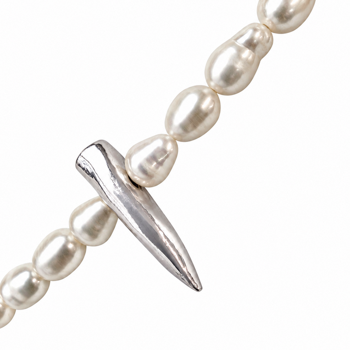 A close-up of a pearl strand bracelet featuring a polished silver spike charm, set against a solid white background.