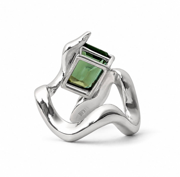 A silver ring with a sculptural, flowing band and a rectangular green gemstone in a bezel setting, shown on a white background.