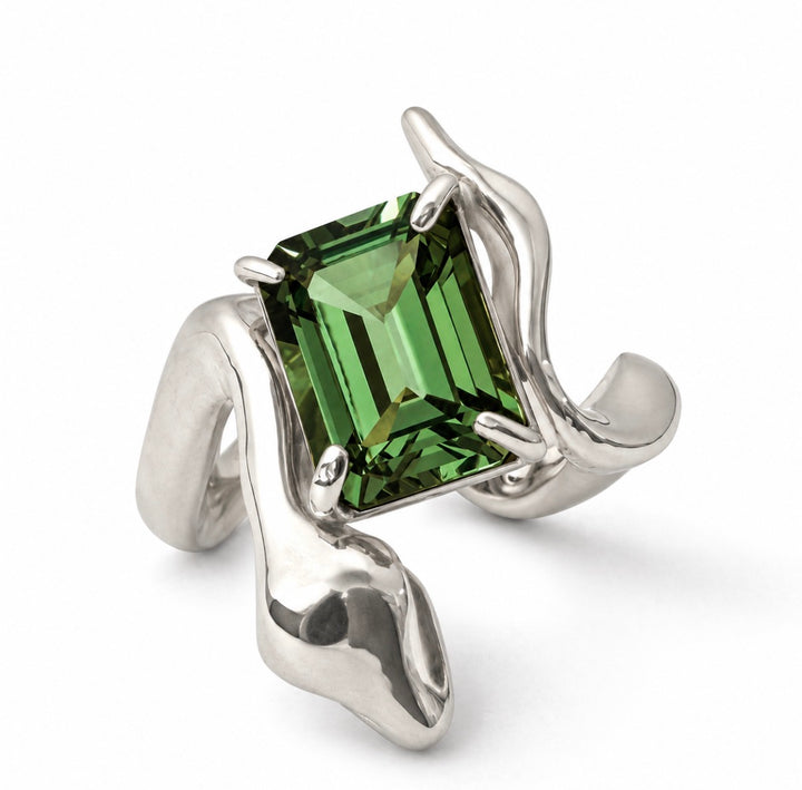 A silver ring featuring a large, faceted emerald-cut green gemstone held in an organic, flowing wrap-style setting, shown on a clean white background.