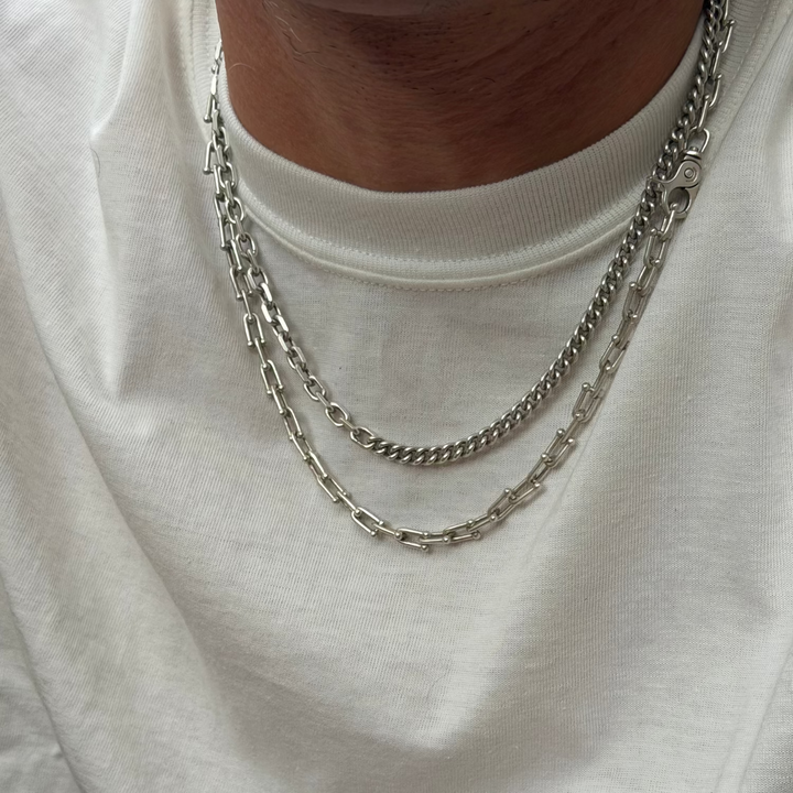 A close-up of a person wearing a layered silver chain necklace over a white crewneck t-shirt.