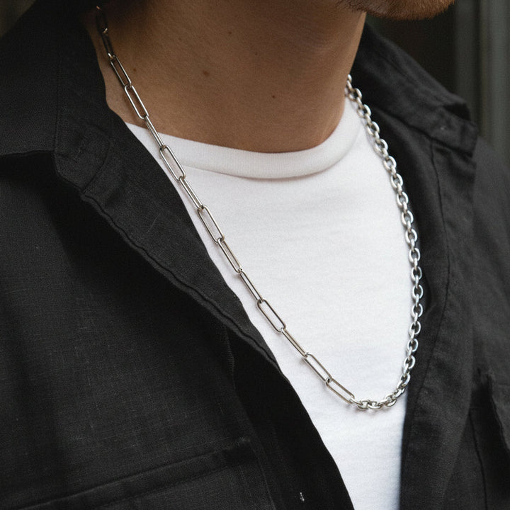 Person wearing a silver chain necklace with a black jacket and white shirt.