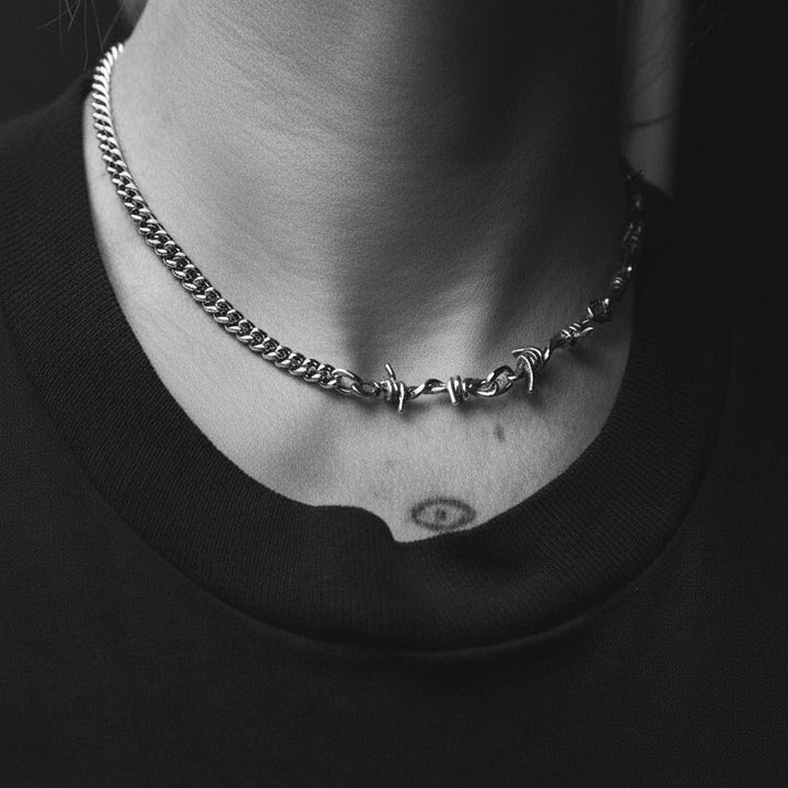 Necklace with barbed wire design worn by a person against a black background