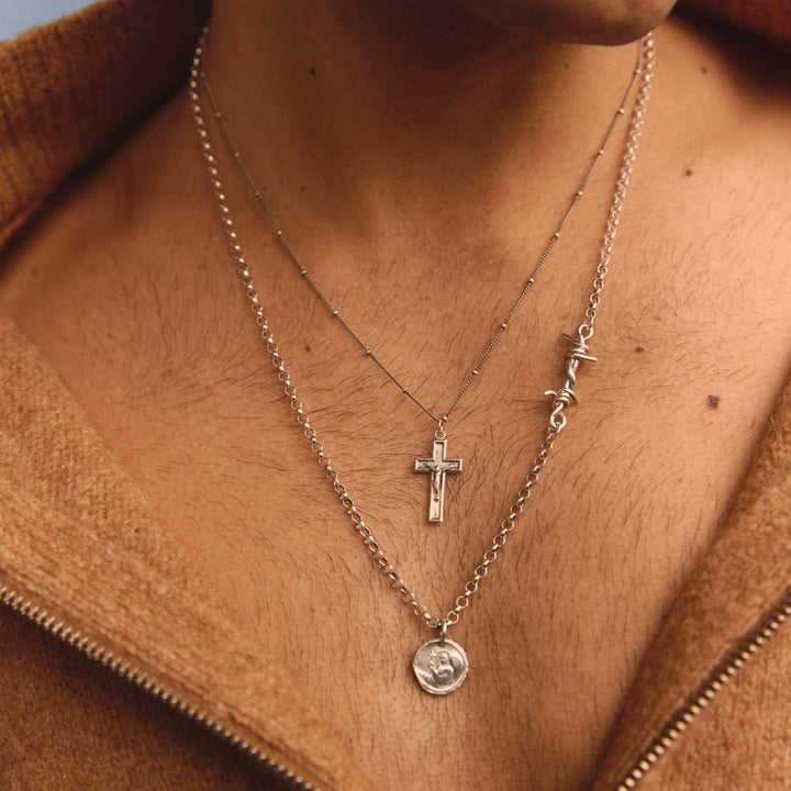 Necklace with a cross pendant worn by a person in a brown jacket.