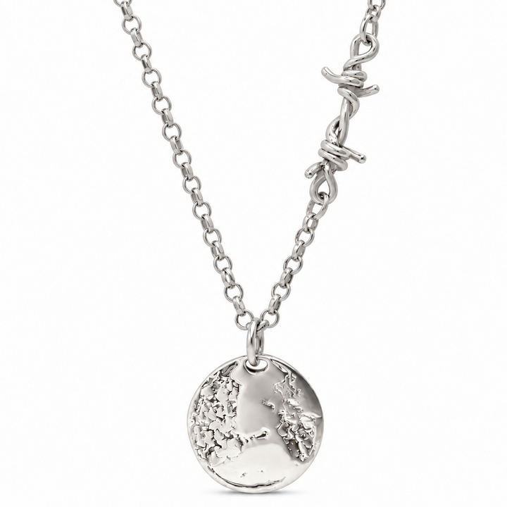 A silver necklace featuring a textured circular pendant with an engraved map design, suspended from a chain with a barbed wire accent clasp, shown against a plain white background.