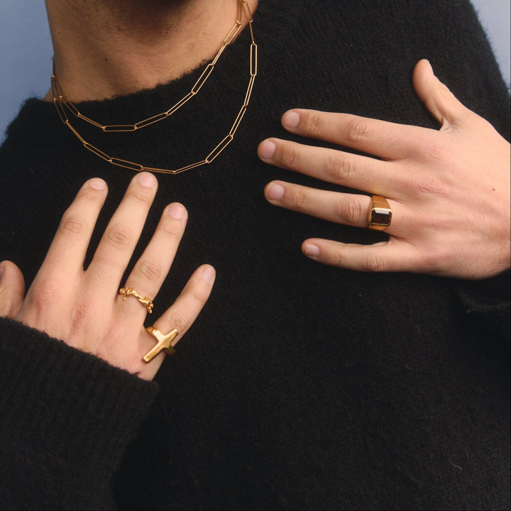 Person wearing gold necklaces and rings on a plain background