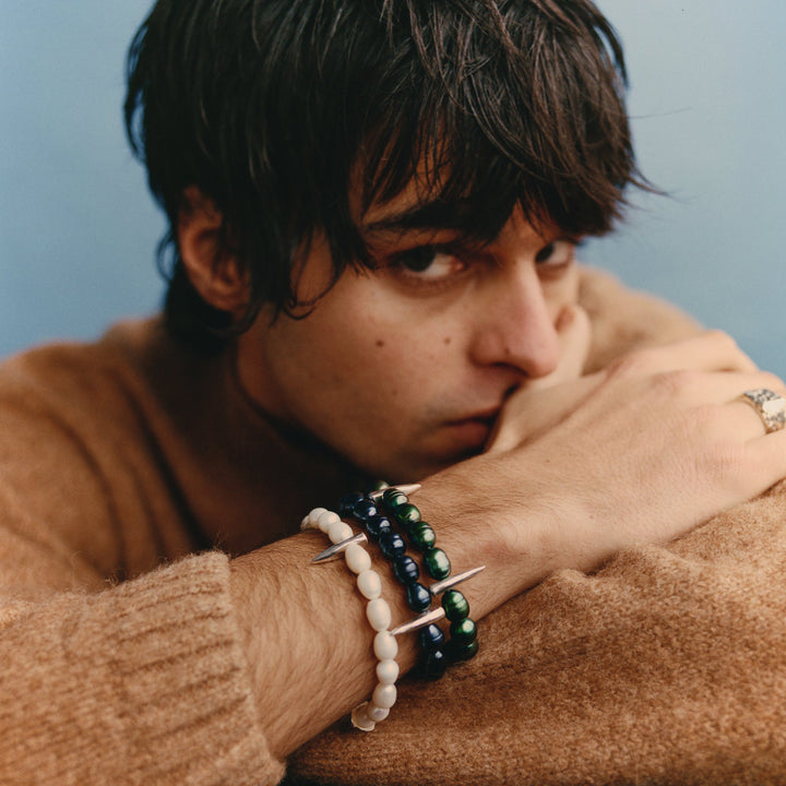 Person wearing a brown sweater with bracelets on a neutral background