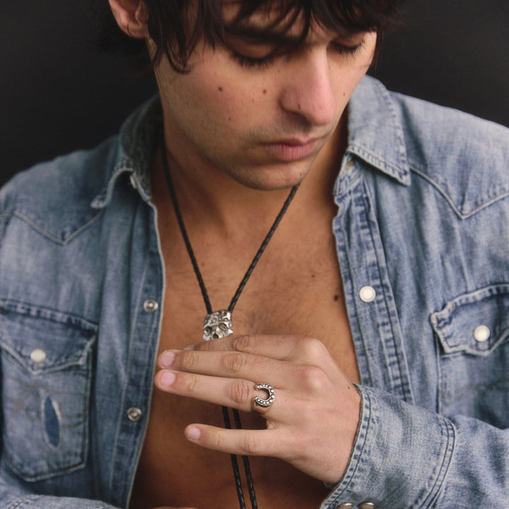 Man wearing a denim jacket with visible jewelry against a dark background