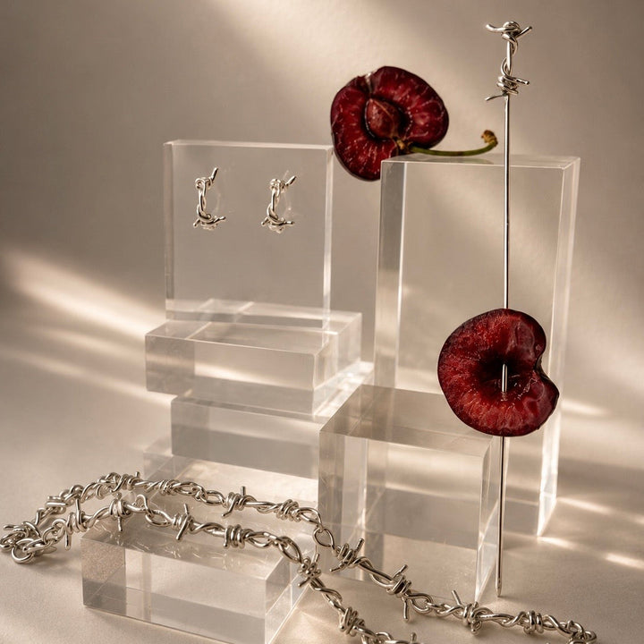 Silver jewelry set including earrings and a necklace on clear stands with a red flower and barbed wire.