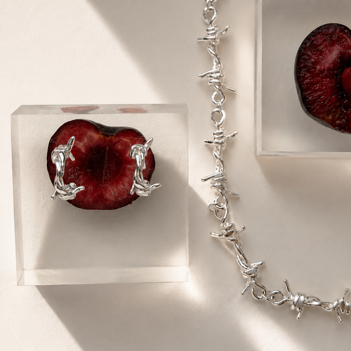Silver necklace and earrings on a white surface with red fruit