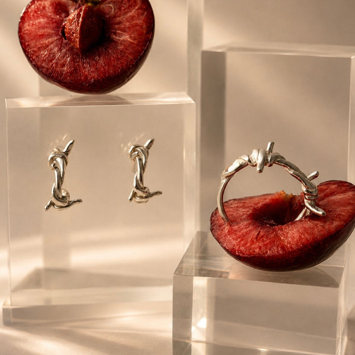 Silver ring and earring set displayed on a cherry with a neutral background