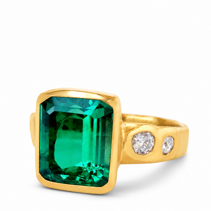 A yellow gold ring featuring a large rectangular emerald-cut green gemstone and two small round clear stones on the band, set against a plain white background.