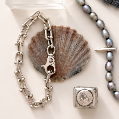 Silver chain bracelet with clasp, shell, and beaded necklace on a white surface
