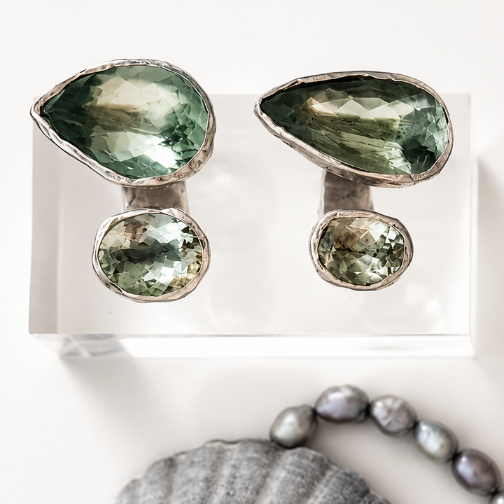 Pair of green gemstone earrings on a white card with a shell and pearl necklace below.