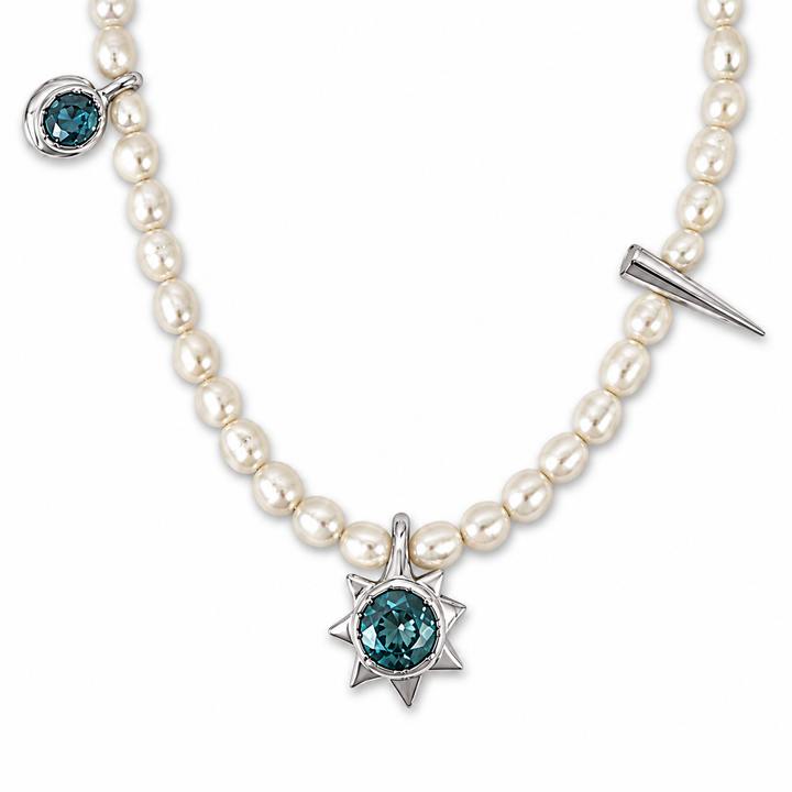 A pearl necklace with a silver-toned starburst pendant featuring a round teal-blue gemstone, a small matching teal-blue stone in a bezel setting on one side, and a pointed spike charm on the other side, shown against a plain white background.