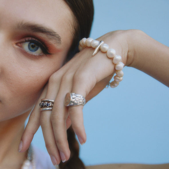 female model resting her head on her hand, wearing our white pearl spike bracelet