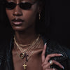 Person wearing sunglasses, layered necklaces, and a black leather jacket against a dark background