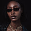 Woman wearing sunglasses and layered necklaces against a dark background