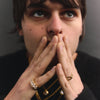 Person with hands over mouth wearing jewelry against a dark background