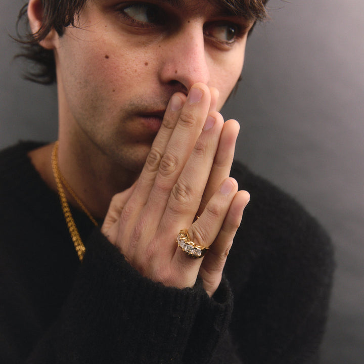 Man wearing a black sweater and gold ring with a blurred background