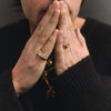 Person with hands clasped together wearing rings, against a dark background