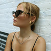 Woman wearing sunglasses and a necklace against a white brick wall