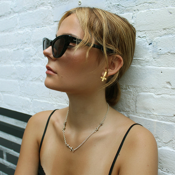 Woman wearing sunglasses and a necklace against a white brick wall
