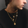 Man wearing a gold necklace with round pendants against a dark background