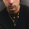 Man wearing multiple gold necklaces with a plain background