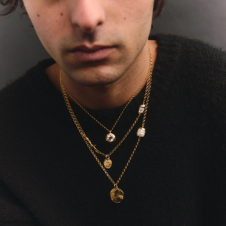Man wearing multiple gold necklaces with a plain background