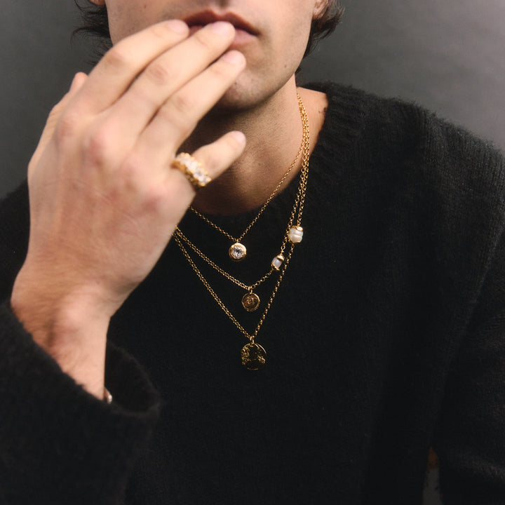 Person wearing gold necklaces and a ring, with a neutral background