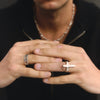 Man wearing sunglasses and a black shirt with a necklace, holding a small cross.