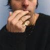 Person wearing a black sweater with a gold CROSS ring on a light blue background
