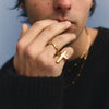 Person wearing a black sweater with a gold ring on a light blue background