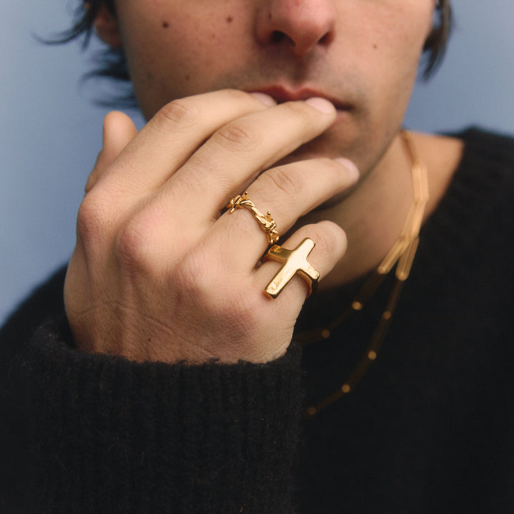 Person wearing a black sweater with a gold ring on a light blue background