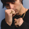 Person wearing gold rings and a black outfit against a blue background