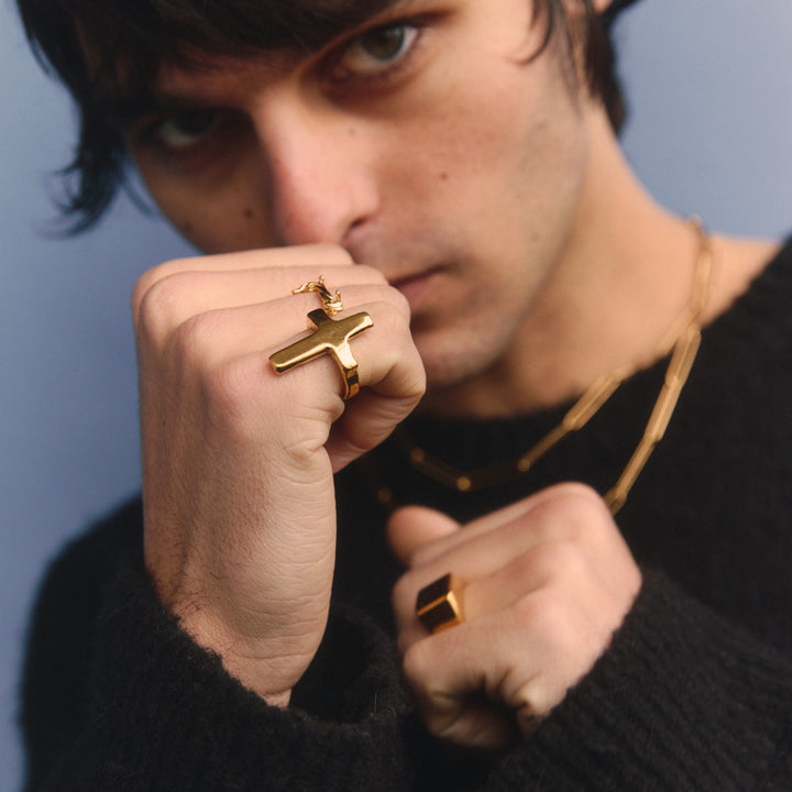 Person wearing gold rings and a black outfit against a blue background