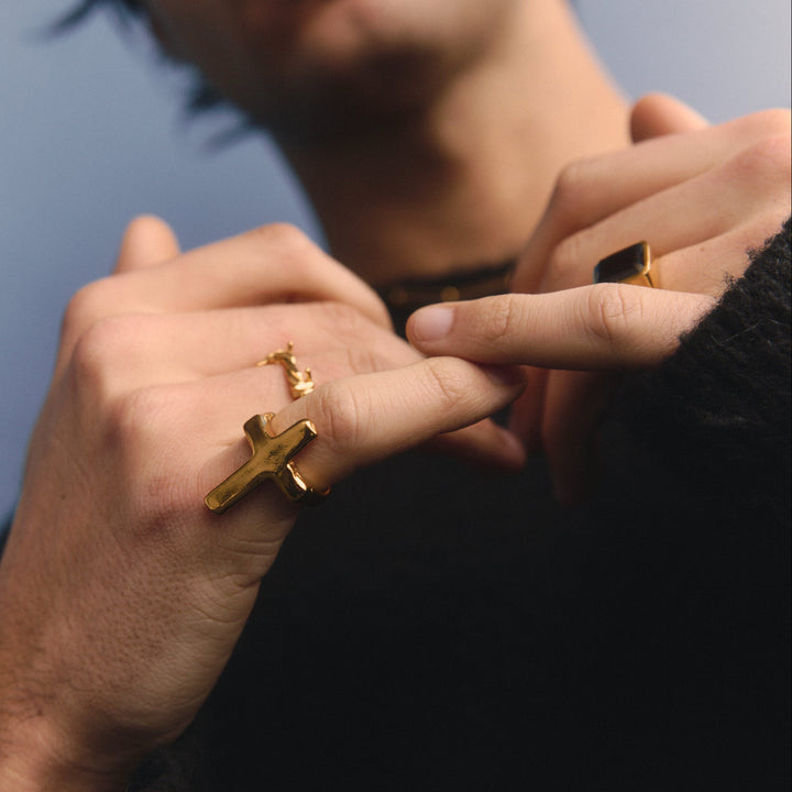 Man wearing a gold cross ring against a blurred background